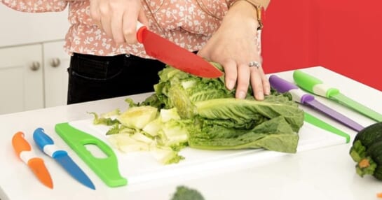 woman cutting lettuce with a colorful knife on a cutting board with more colorful knives around it